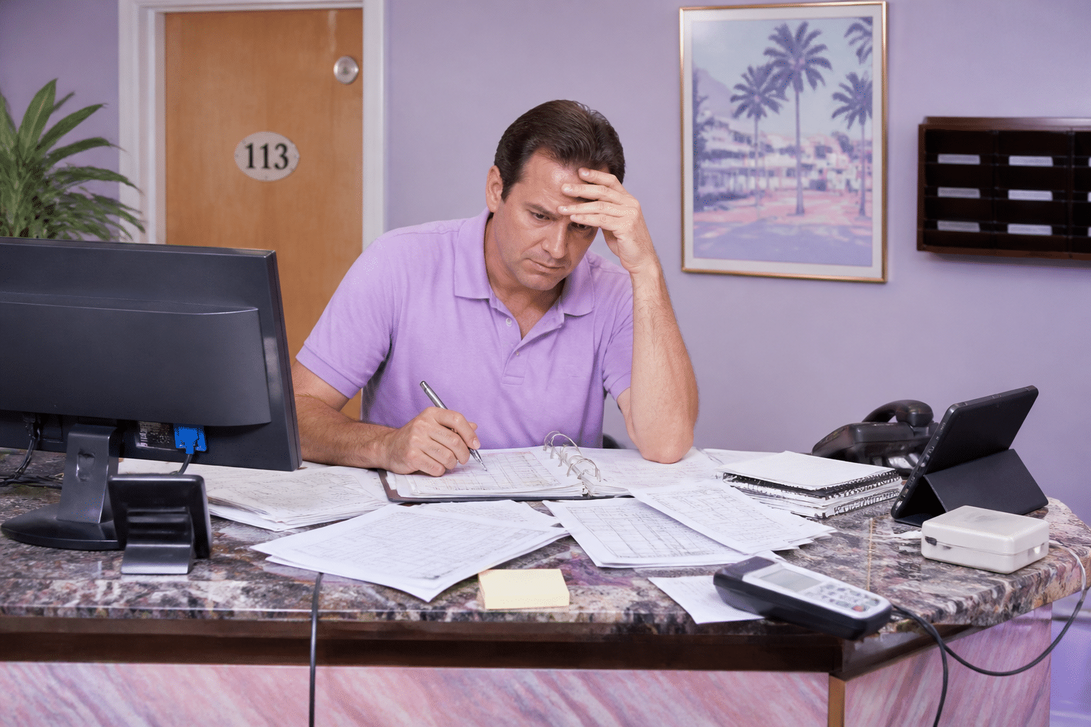 Overwhelmed motel front desk worker juggling multiple paper logs, spreadsheets, and disconnected devices